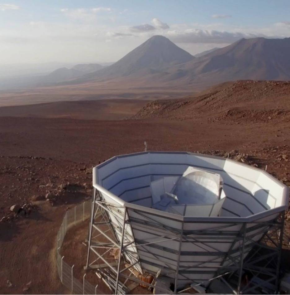 A giant telescope points upwards to the sky, surrounded by desert sands, with a mountain on the horizon.