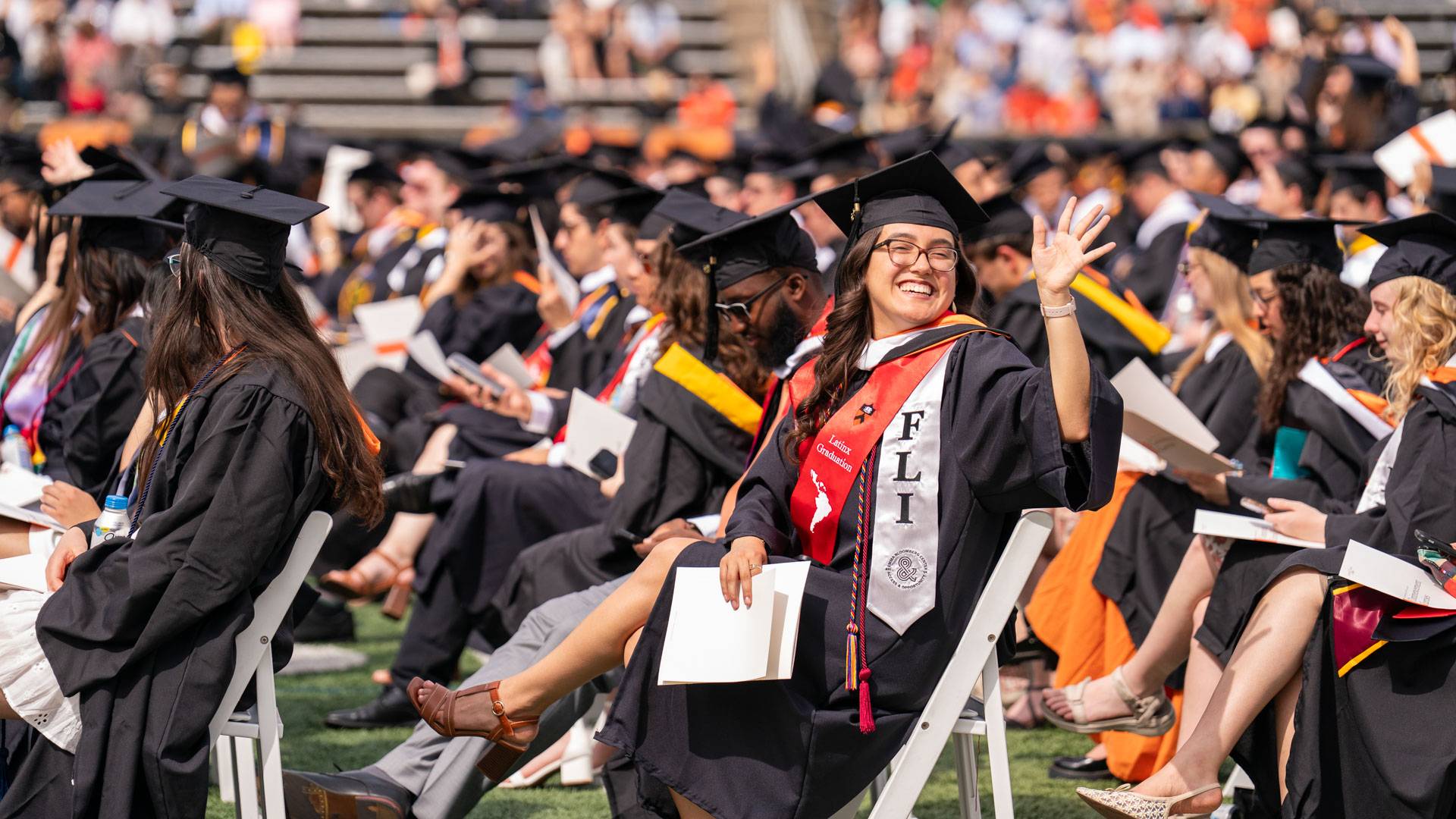 A graduating senior waves from her seat on the field.
