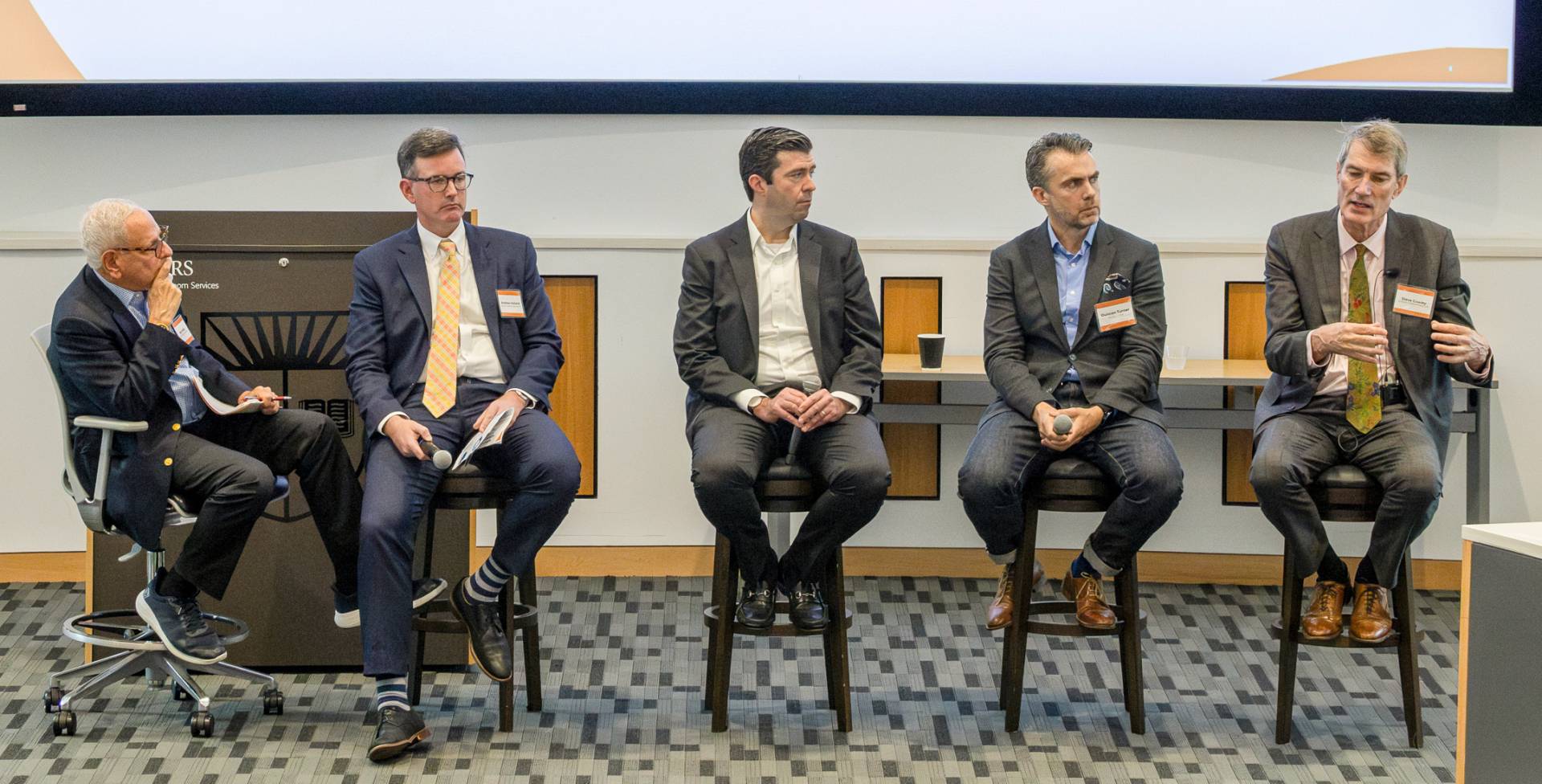 Moderator Matt Miller addresses a panel of four speakers seated on the summit stage. 