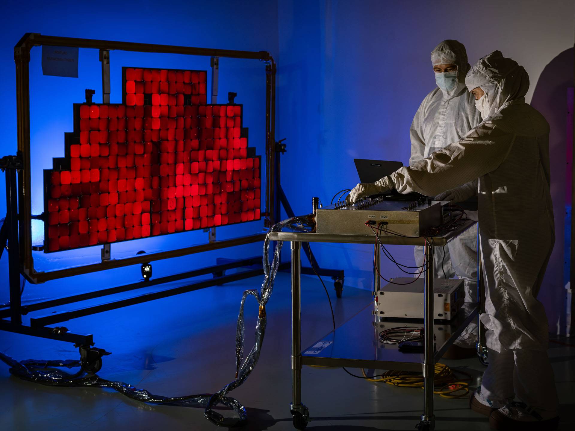 Engineers in white coveralls shine a light at solar panels.