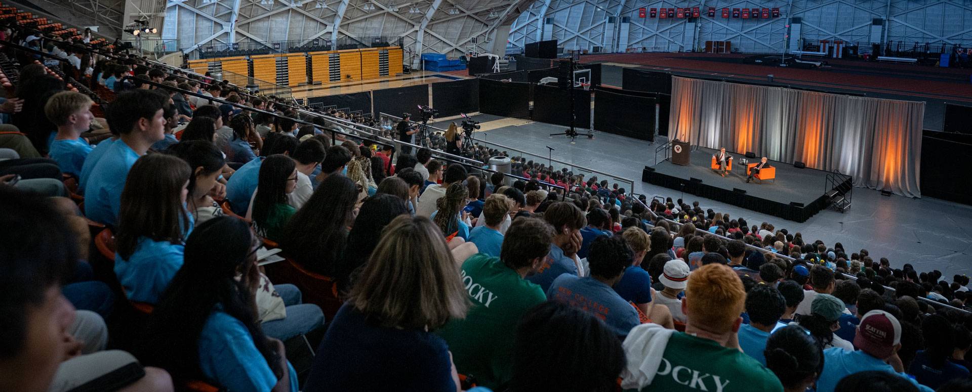 A crowd of students listen to two speakers.