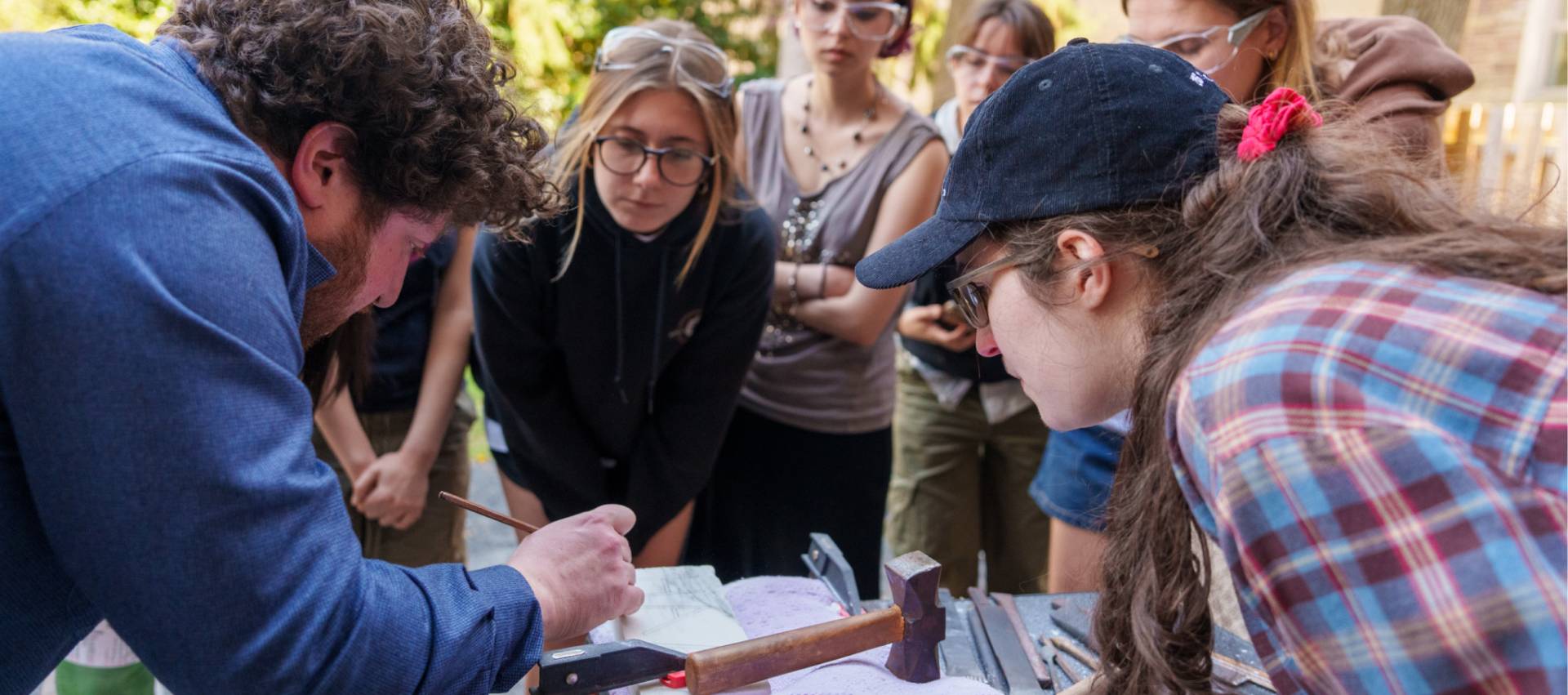 A group of students inspecting plans with hammer and chisel nearby