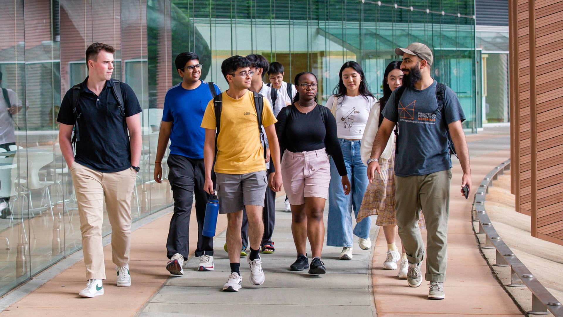 Graduate students walking in a group past a contemporary campus building.