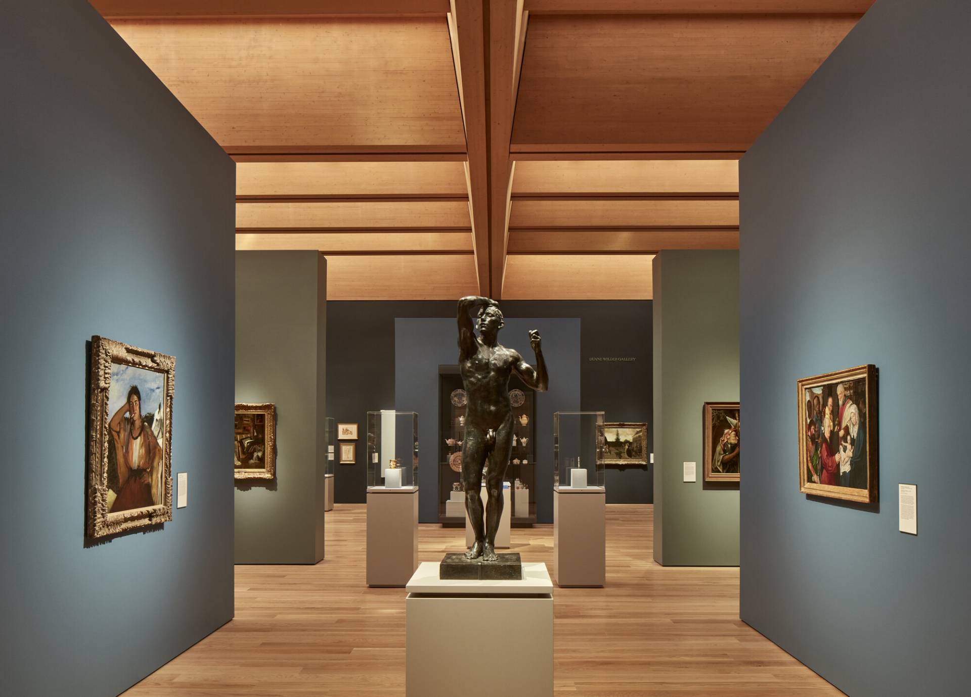 Dark patina bronze sculpture of a full figure of a nude male, on a podium among paintings in the pavilion of European art in Princeton University Art Museum