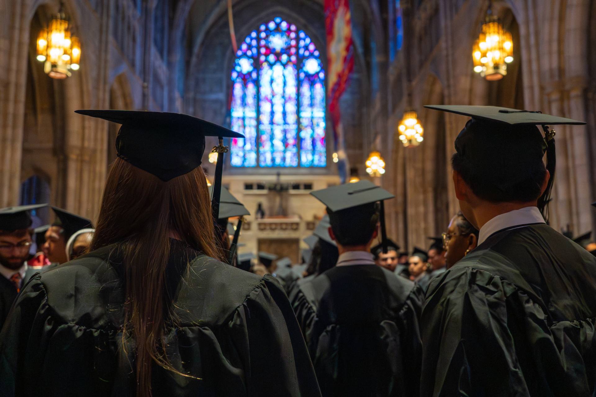 Graduating seniors walk toward a stained-glass window.