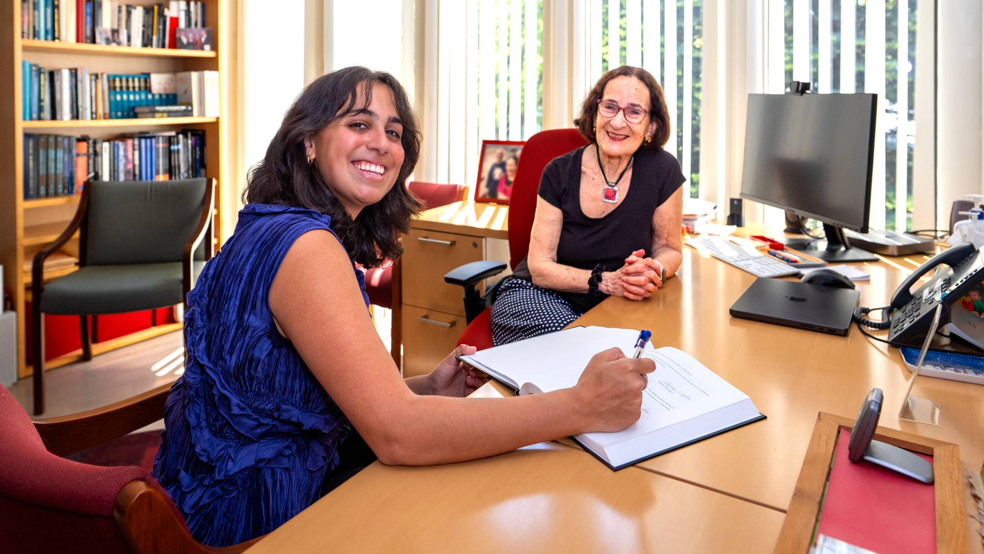 Varughese and Bahcall sit at a desk in Bahcall's office