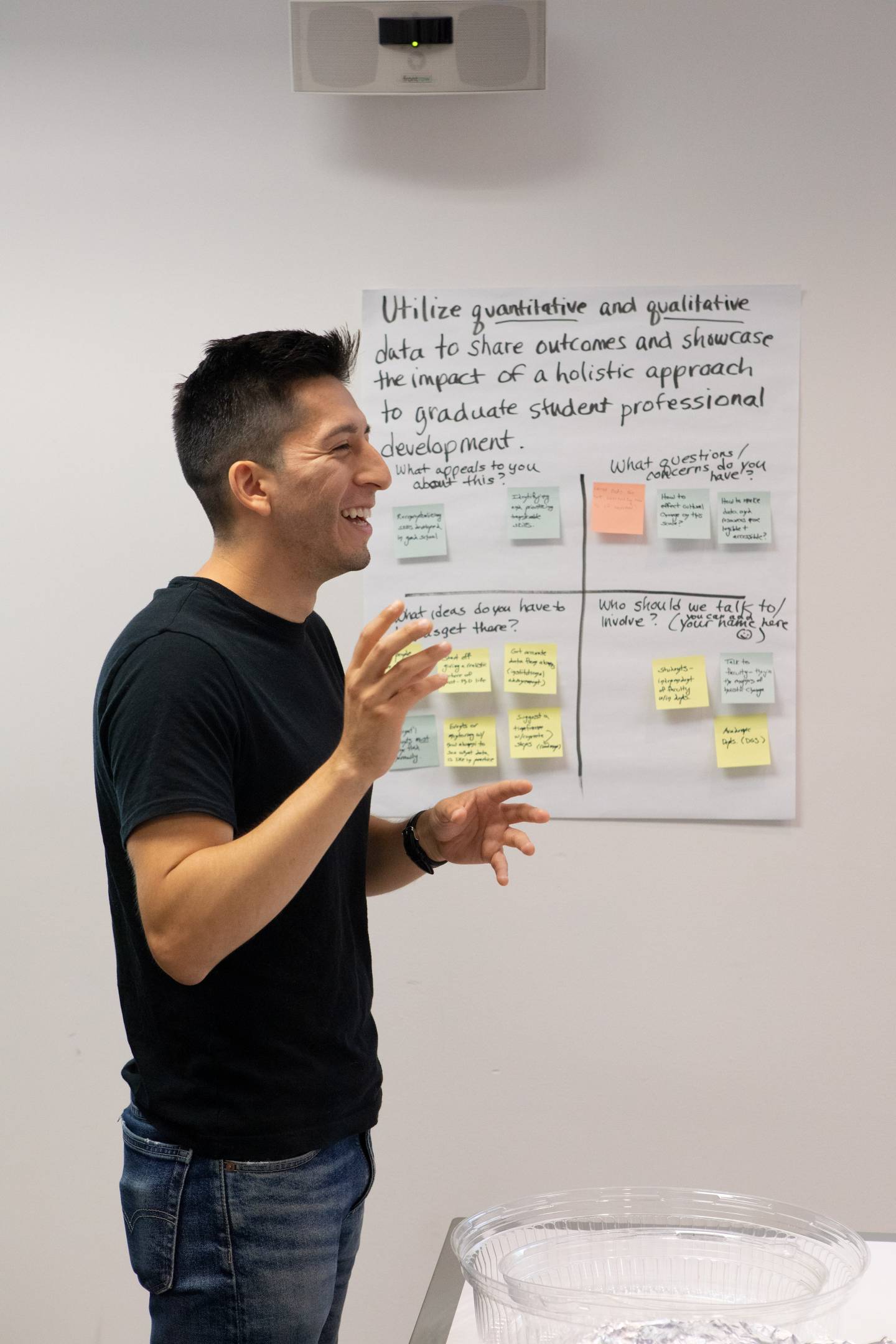 A student gesticulates and speaks with a handwritten chart in the background