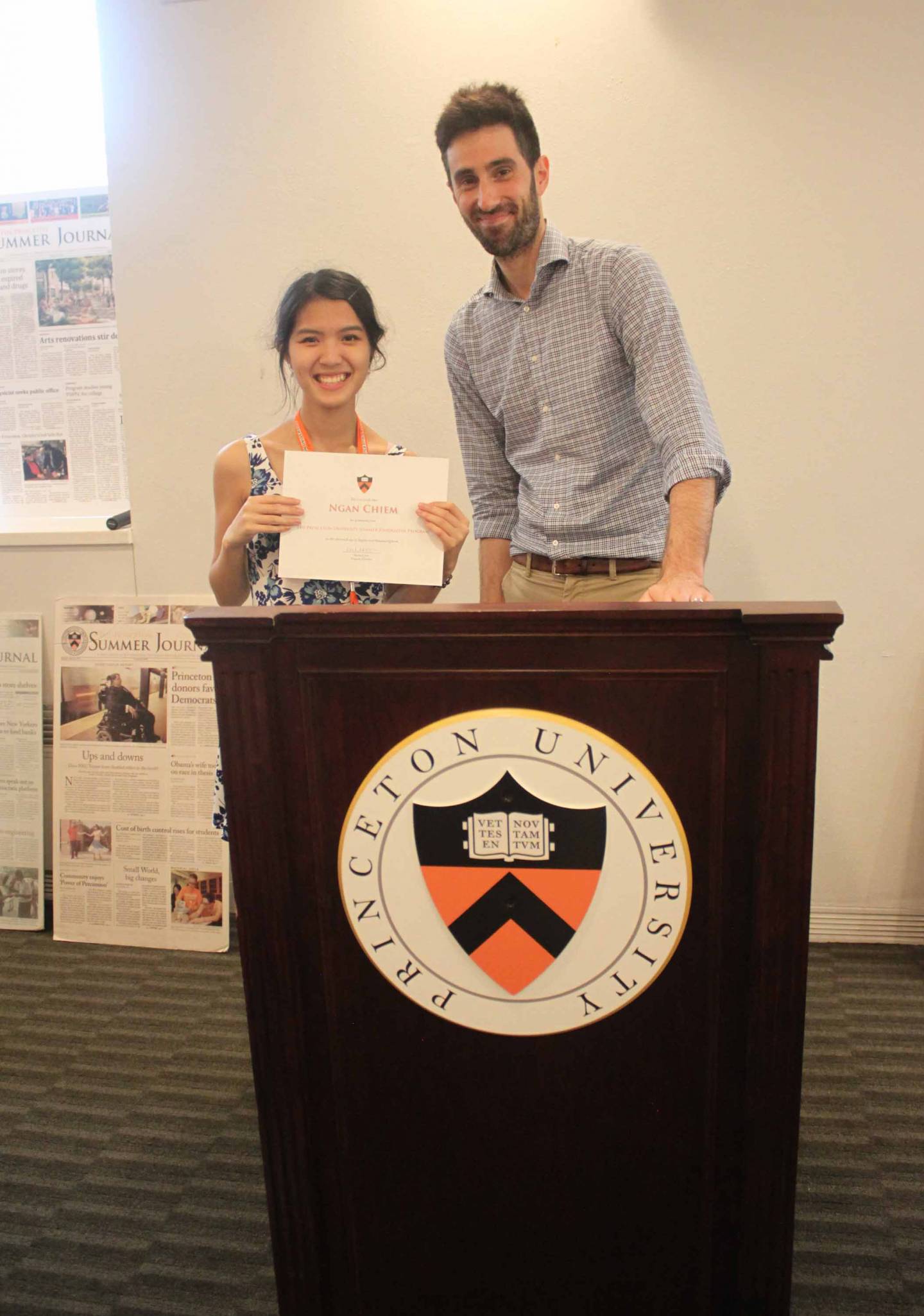 Ngan Chiem holds a certificate while standing next to Richard Just at a podium