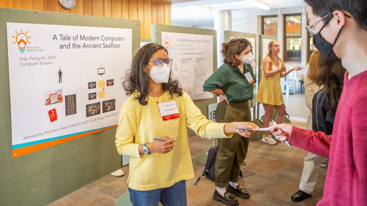 A student standing in front of her research poster hands a card to another person