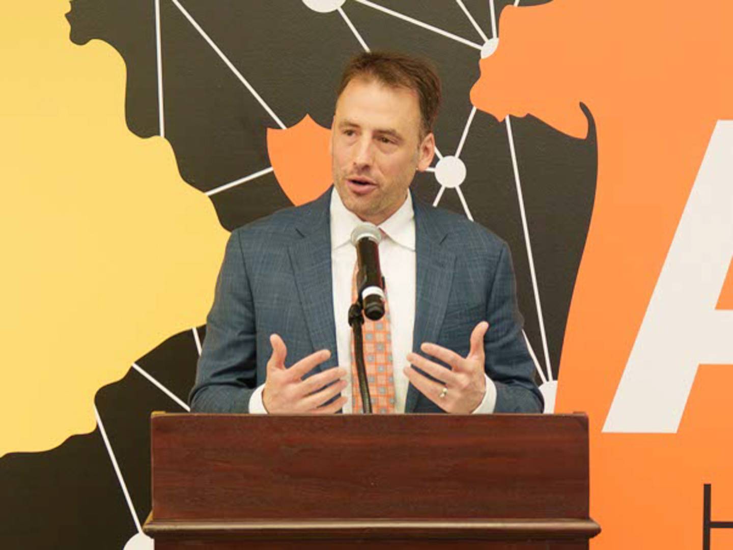 A man speaks in front of the NJ AI Hub logo, which shows the Princeton shield connected to other points across New Jersey.