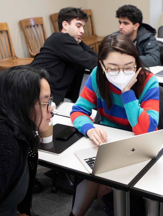 students having a discussion while looking at a laptop