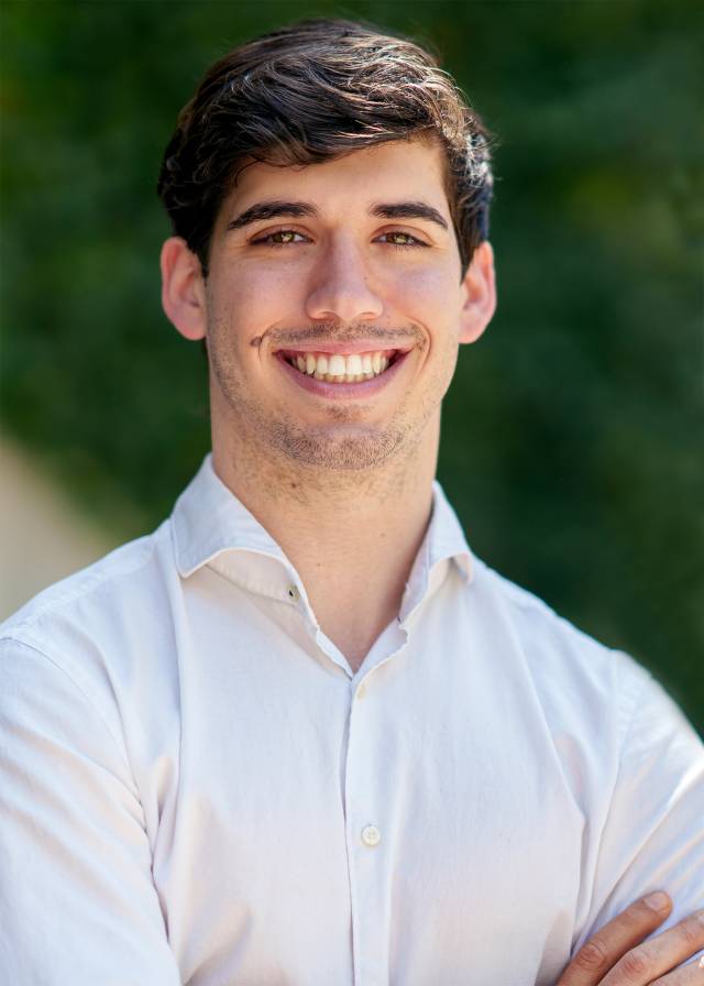 A smiling young man with brown hair and eyes in a white collared shirt.