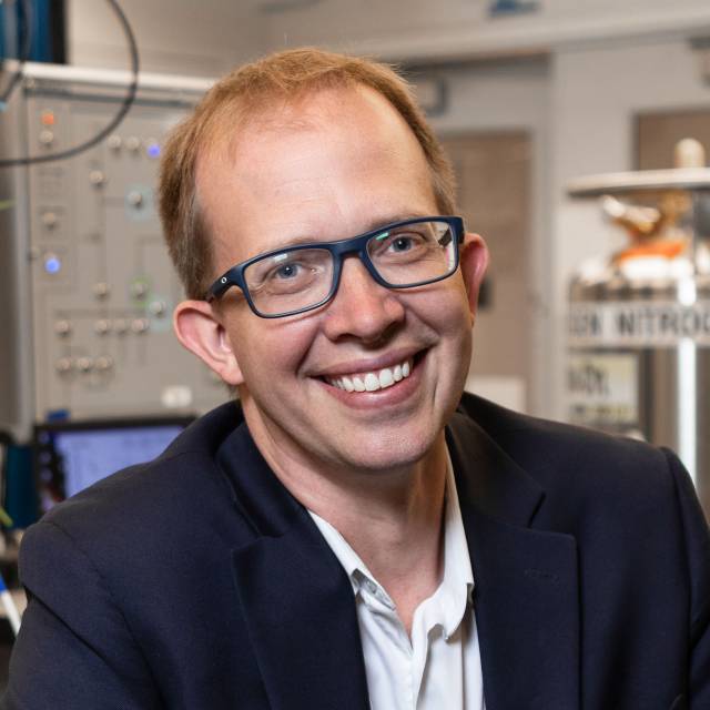 Andrew Houck smiles in a suit jacket and glasses